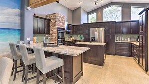A modern kitchen with dark cabinetry, a central island, and a brick fireplace. - Huge Home w/ Pool Table Near St Pete Beach! (Seminole)