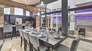 A modern kitchen with dark cabinetry, a brick accent wall, and a dining area with a large table set for six. - Huge Home w/ Pool Table Near St Pete Beach! (Seminole)