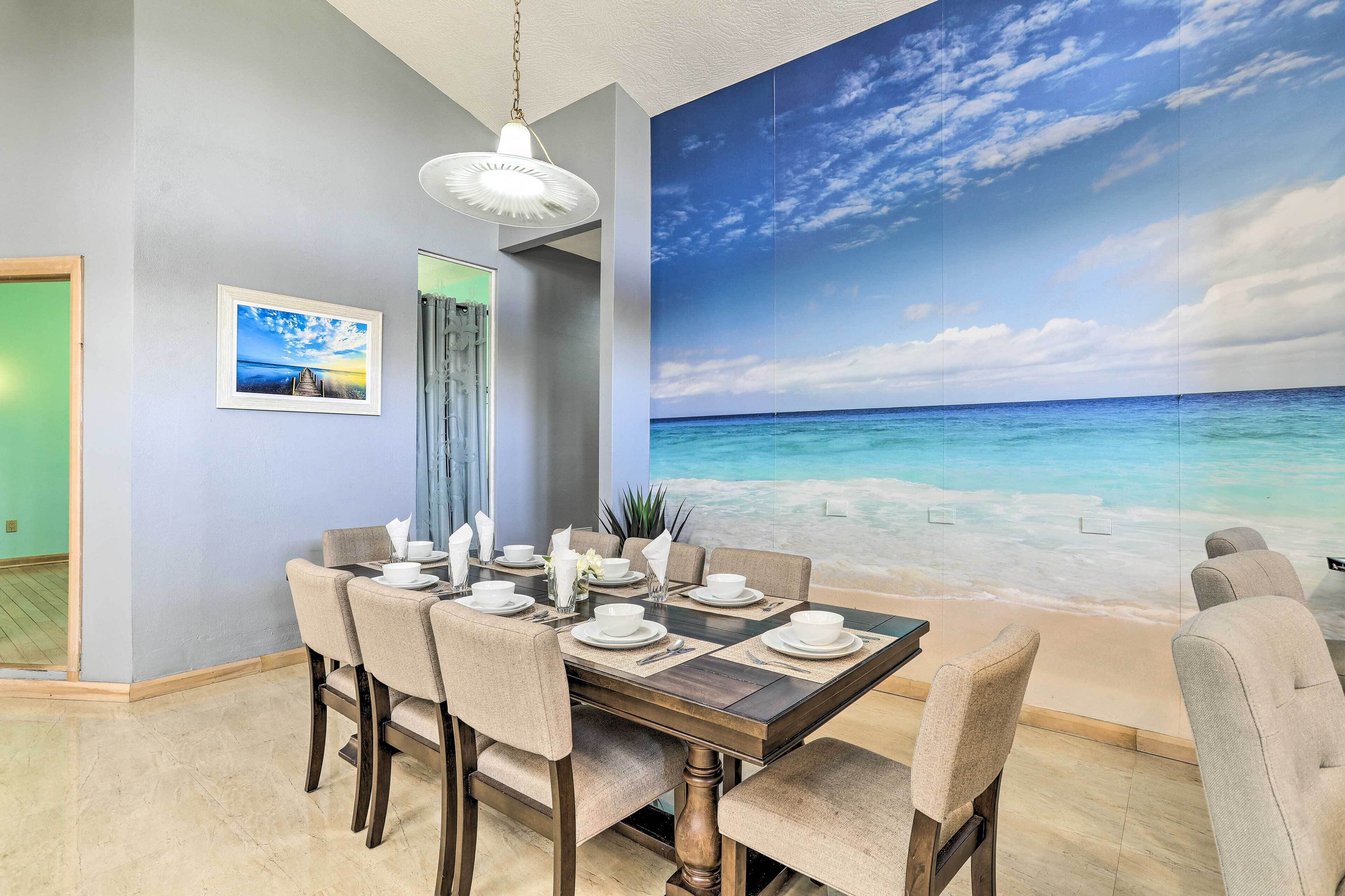 Comedor con un mural de playa, un cuadro enmarcado y una lámpara de araña moderna.