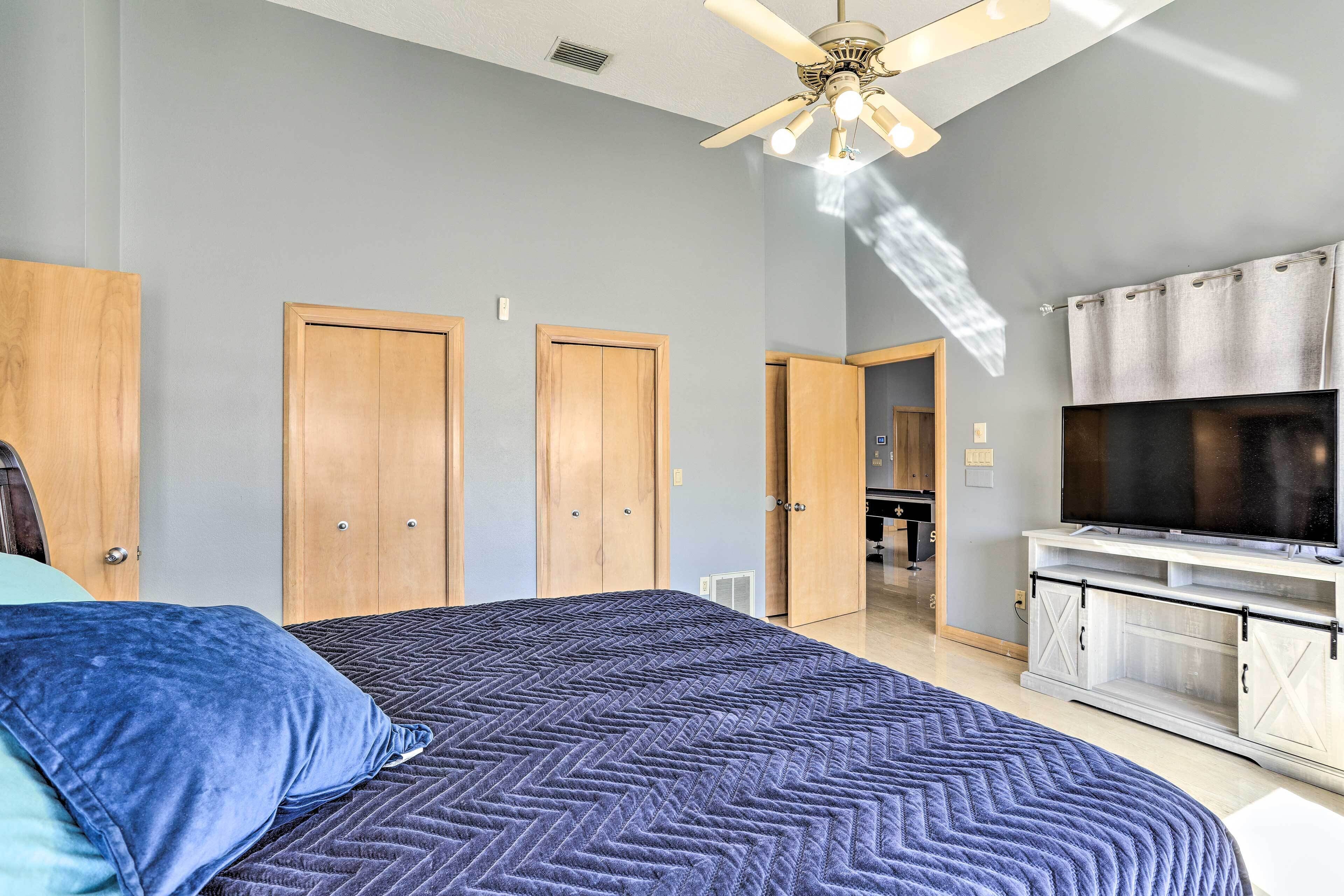 Une chambre à coucher avec un lit, un ventilateur de plafond, des armoires en bois et un téléviseur posé sur un meuble.