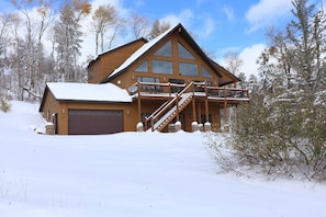 A large wooden cabin with a garage, a balcony, and a staircase leading to the upper floor.