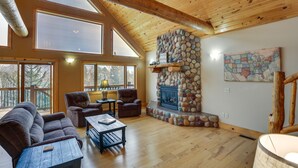 A spacious living room with a stone fireplace, large windows, and a wooden ceiling. - Spacious Terry Peak Cabin < 1 Mi to Ski Lift (Lead)
