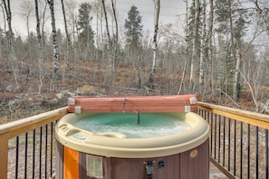 A hot tub on a wooden deck with a forest backdrop.