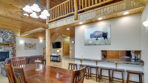A spacious dining area with a wooden table and chairs, a stone wall with a fireplace, and a mounted television. - Spacious Terry Peak Cabin < 1 Mi to Ski Lift (Lead)