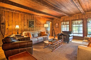 A cozy log cabin interior with a leather sofa, a wooden coffee table, and a fireplace. - Vintage Schroon Lake Farmhouse w/ Private Beach! (Schroon Lake)