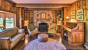 A cozy, rustic living room with a fireplace, leather armchairs, a sofa, and a wooden desk. - Vintage Schroon Lake Farmhouse w/ Private Beach! (Schroon Lake)