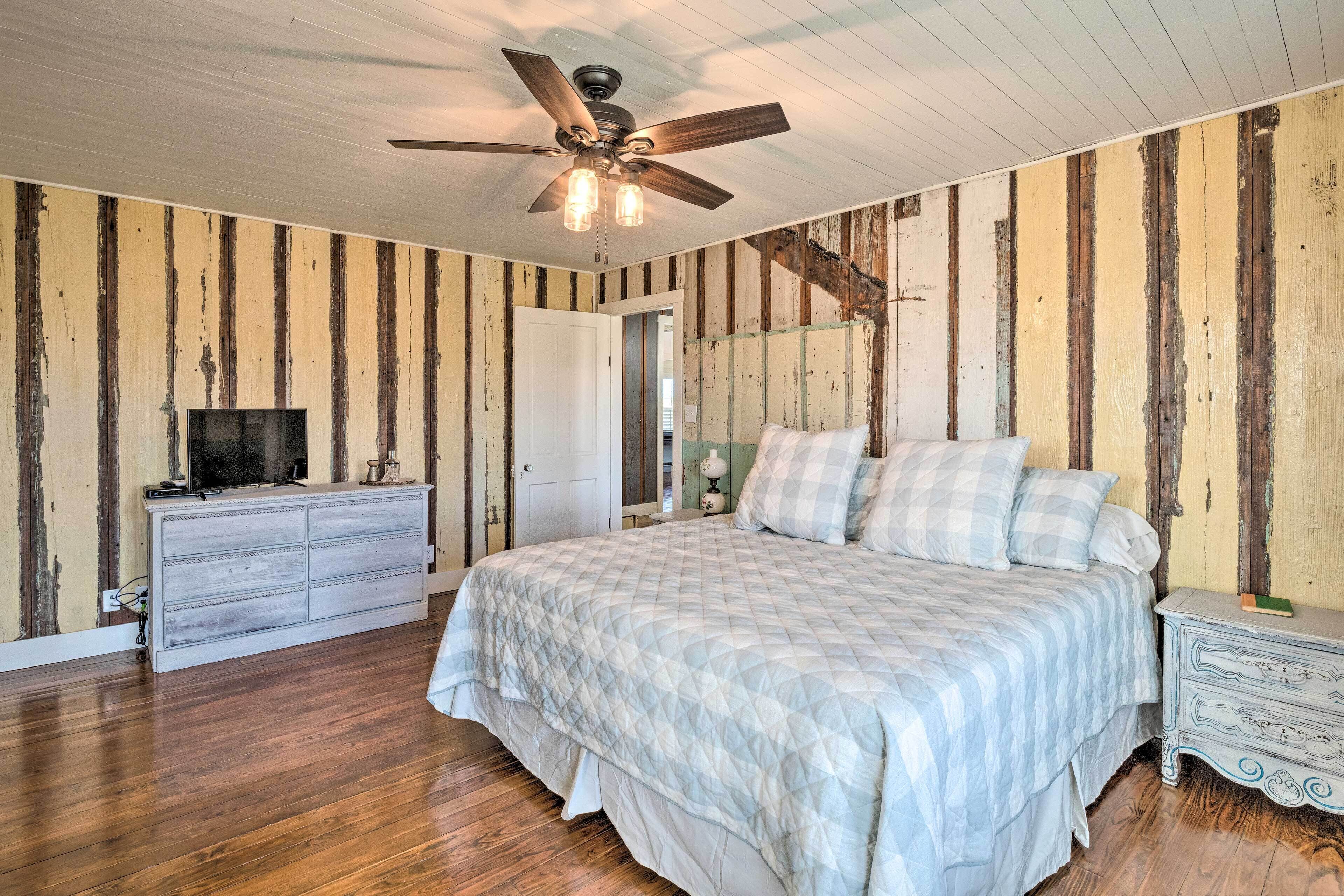 A bedroom with a bed, a dresser, a television, and a ceiling fan.