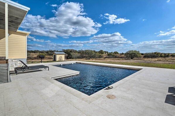 Una piscina rectangular con un borde de baldosas, una tumbona y una estructura pequeña al fondo.