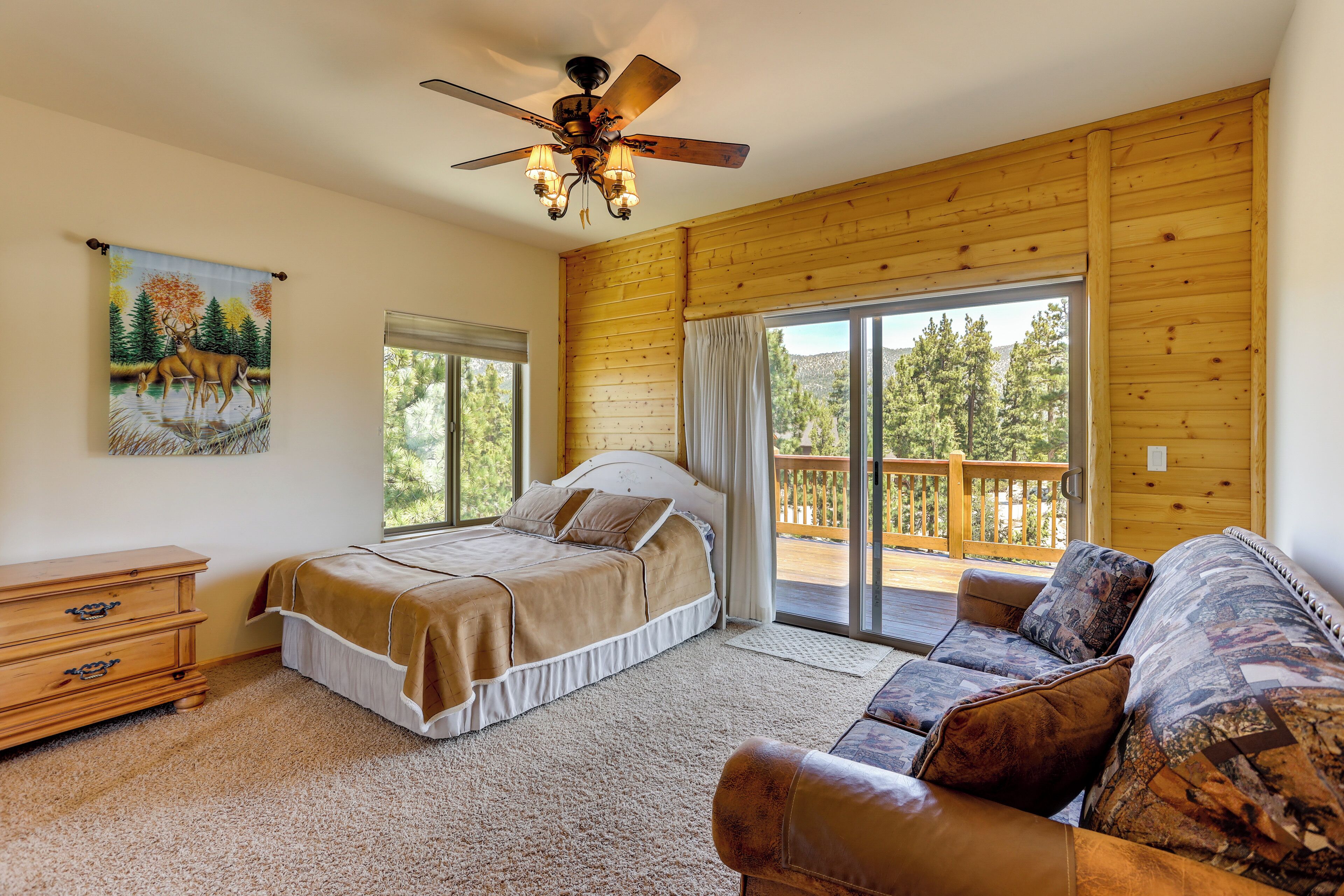 A bedroom with a bed, a dresser, a sofa, and a balcony with a view of trees.
