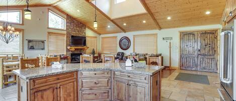 A spacious kitchen with a large island, wooden cabinets, and a stone fireplace.