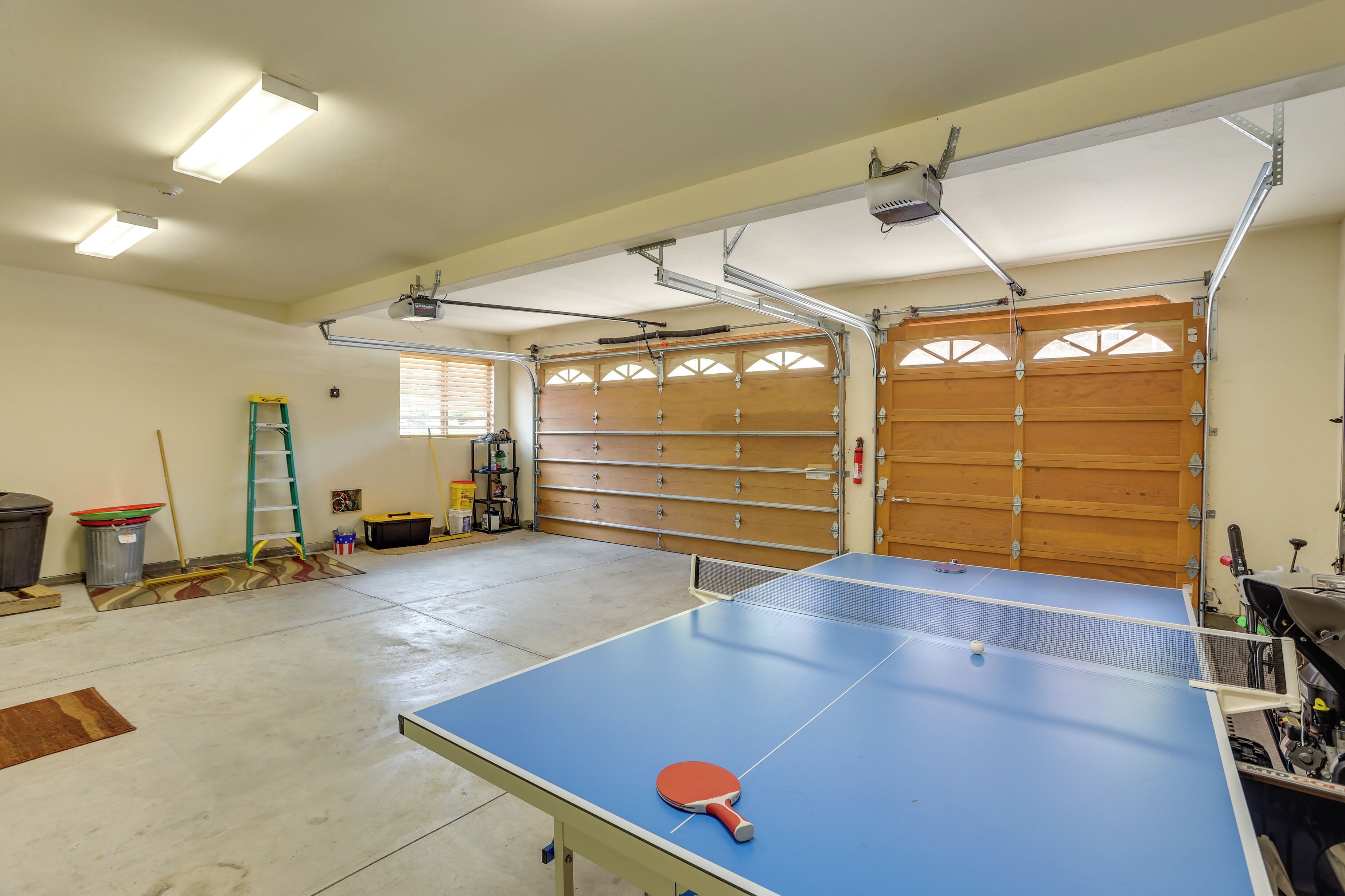 Un grand espace intérieur comprenant une table de ping-pong, une échelle et une porte de garage.
