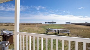 A porch with a white railing overlooking a grassy field with a picnic table and grill. - Historic Hoopersville Getaway on Chesapeake Bay! (Fishing Creek)