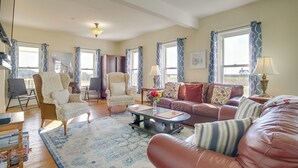 A spacious living room with a large sofa, armchairs, and a coffee table. There are multiple windows with curtains, a chandelier, and a rug. - Historic Hoopersville Getaway on Chesapeake Bay! (Fishing Creek)