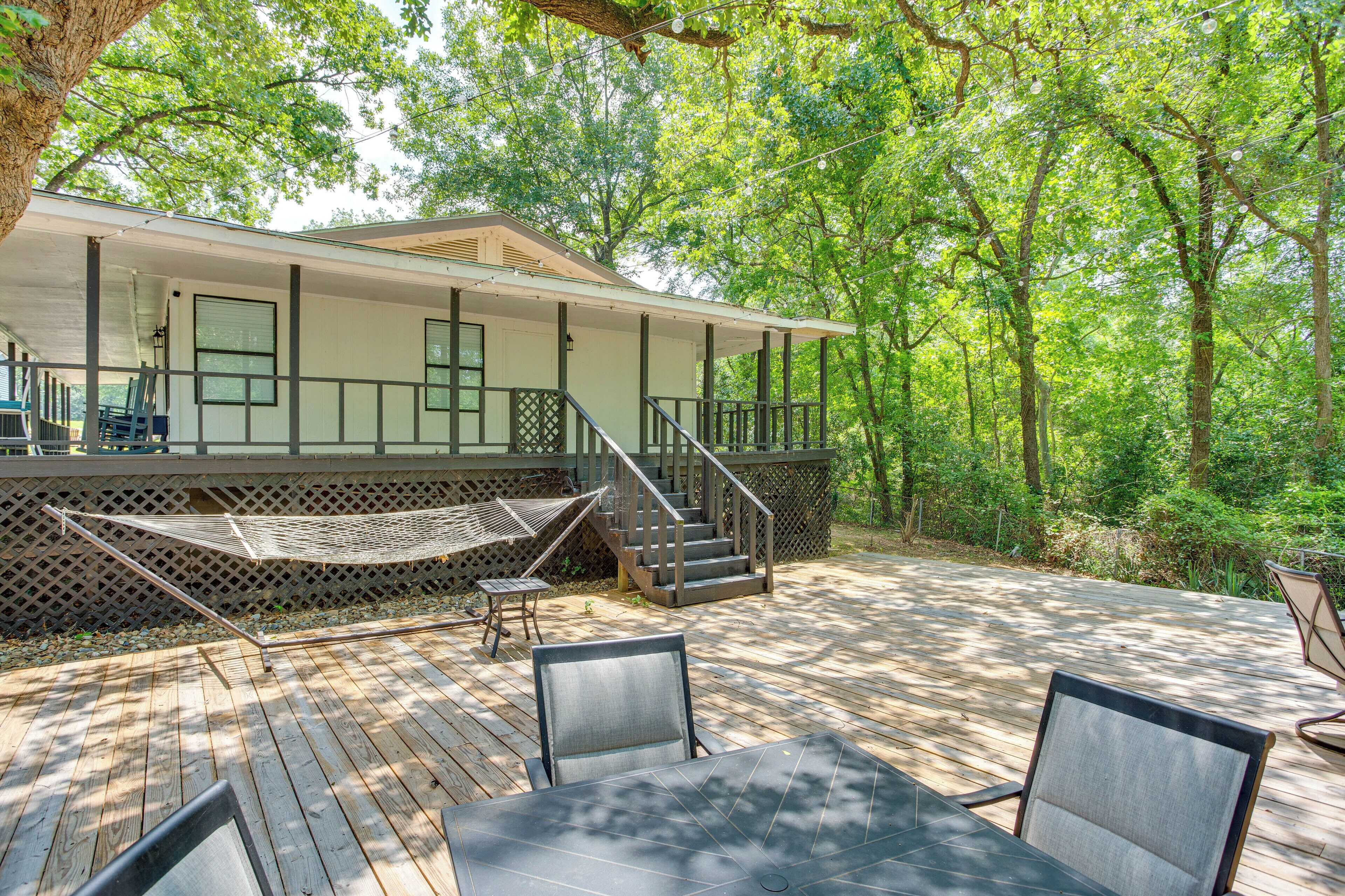 A wooden deck with outdoor furniture, a hammock, and a staircase leading to a covered porch.