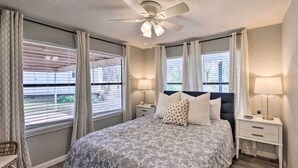 A bedroom with a large bed, two bedside tables with lamps, a ceiling fan, and a view of the outdoors through the windows. - Lake View & Decks: Pet-friendly Mabank Home (Mabank)