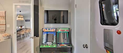 A room with a door leading to a dining area, two arcade machines labeled 'Rampage' and 'Centrode', and a white door with a colorful stripe.