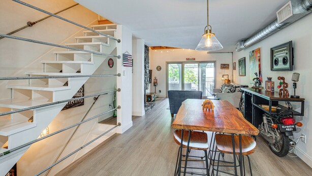 Um interior moderno com uma mesa de jantar de madeira, banquetas de bar, uma escada com grades de metal e uma motocicleta.