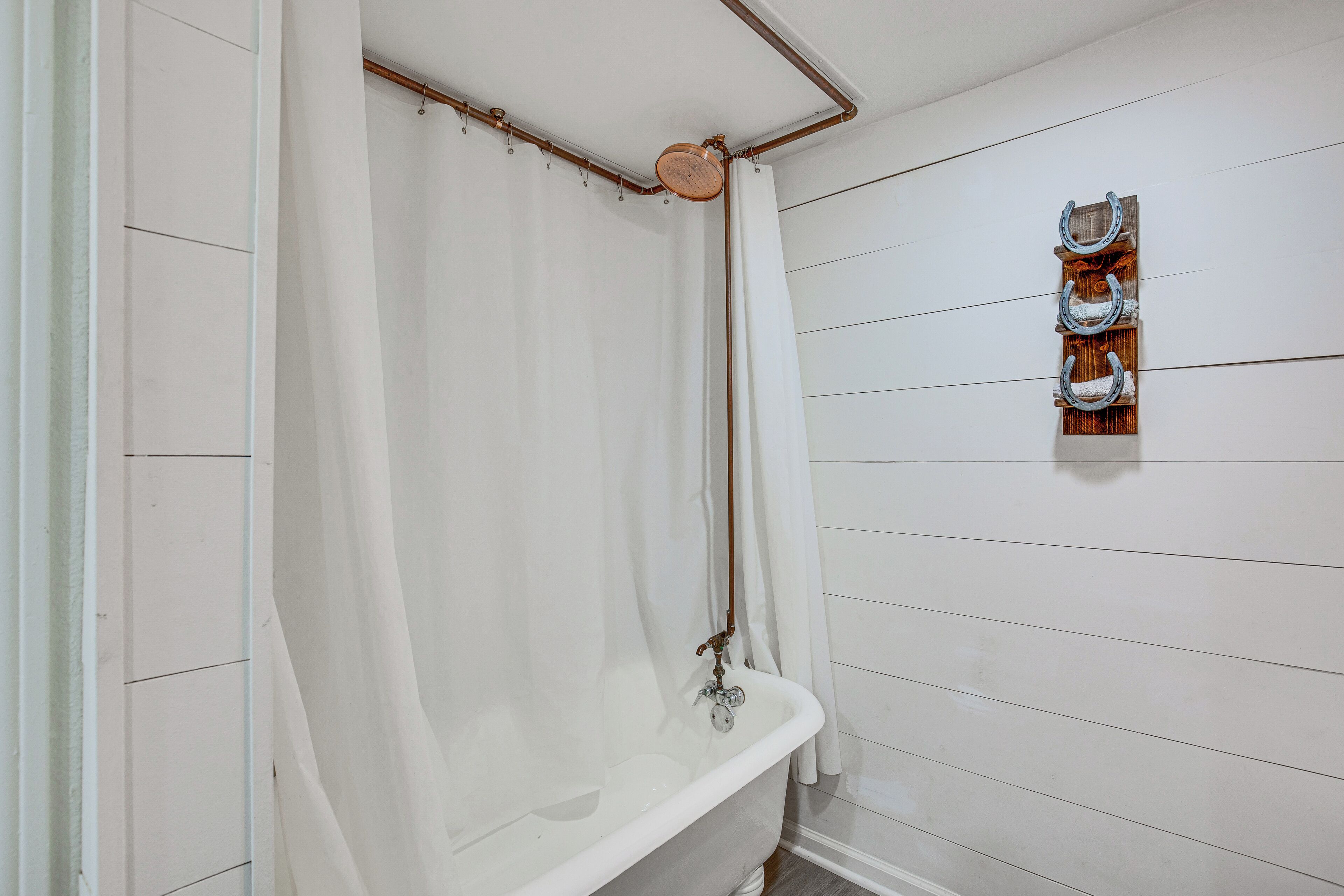 A bathroom with a white bathtub, a wooden wall-mounted towel rack, and a white shower curtain.