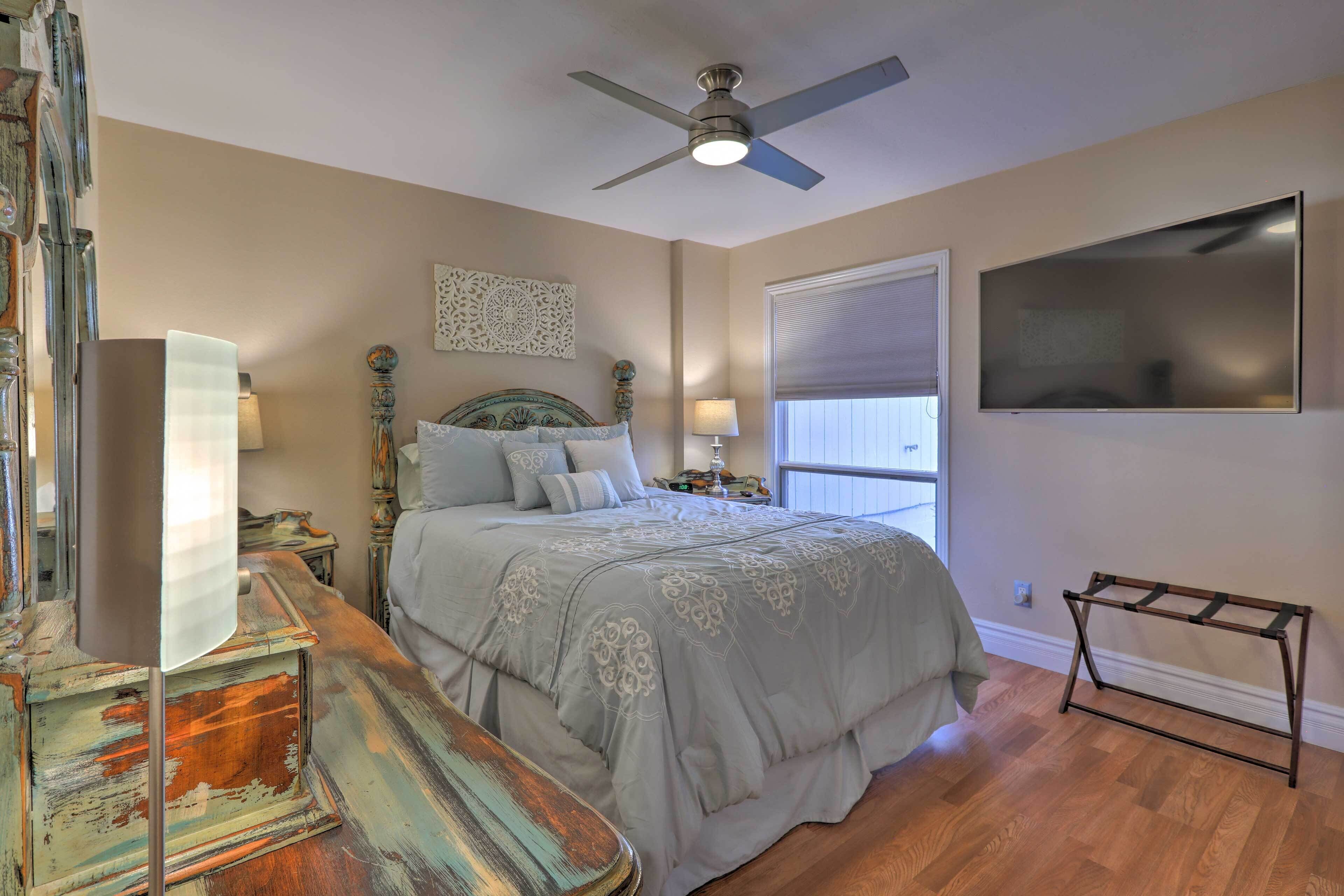 A bedroom with a bed, a ceiling fan, a TV, and a window with blinds.