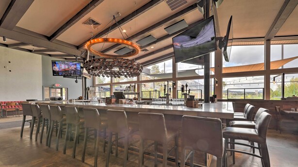 A spacious bar area with a long counter, multiple stools, and a large screen displaying a program. - Flagstaff Townhome w/ View, Country Club Amenities (Flagstaff)