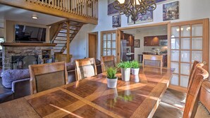 A spacious dining area with a large wooden table, several chairs, and potted plants. A staircase with a wooden railing leads to an upper level.