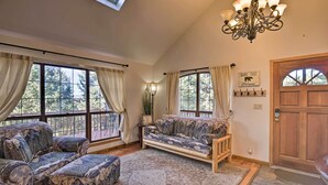 A cozy room with a large window, a sofa, a bench, and a chandelier.