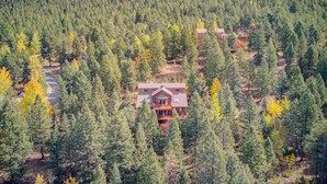 A large, two-story lodge surrounded by dense forest, with a clear road leading to it.