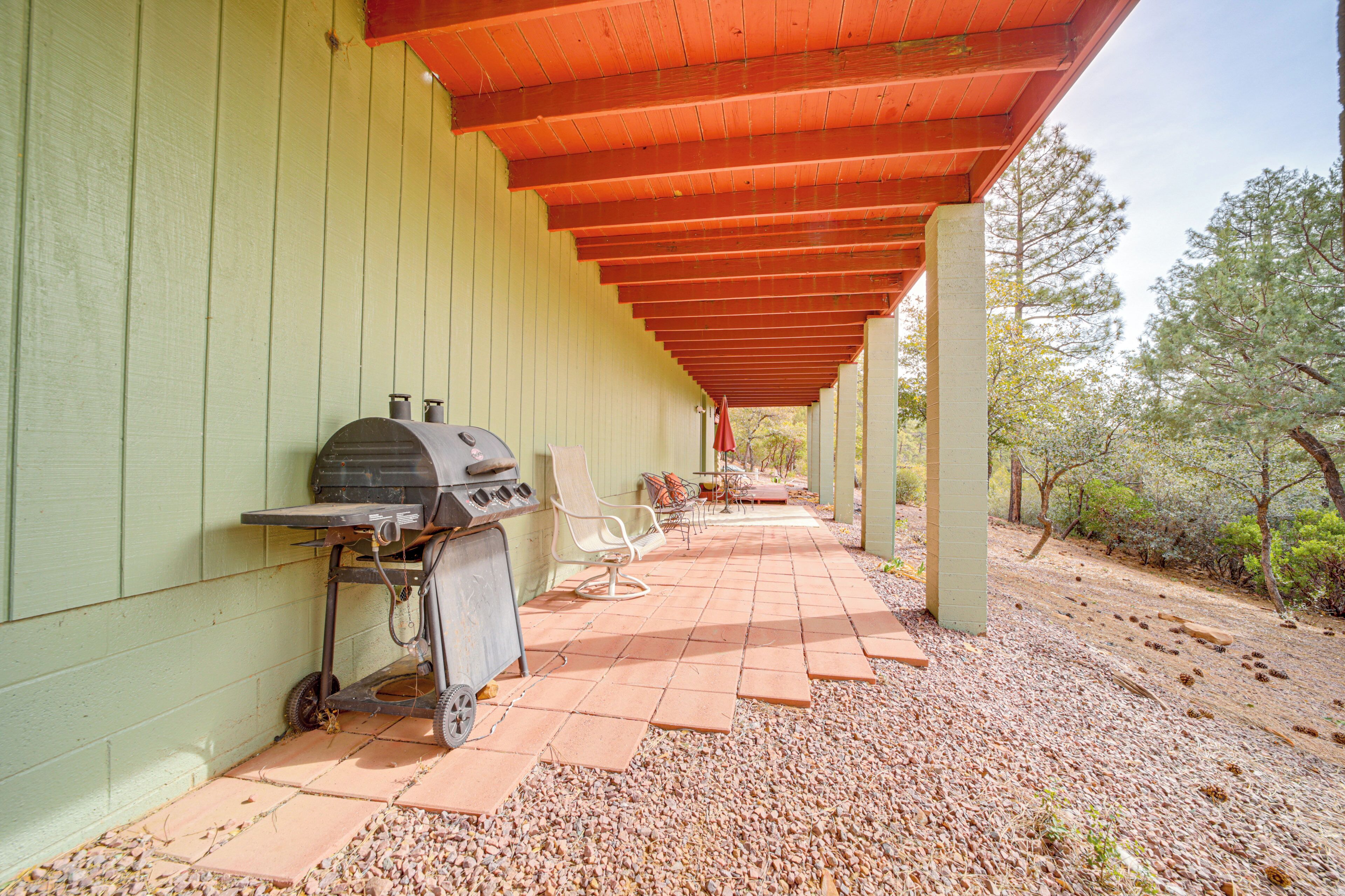 Un patio couvert avec un barbecue, des sièges et une vue sur les arbres.