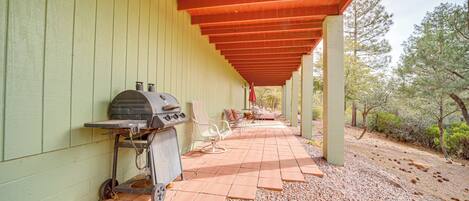 Un patio couvert avec un barbecue, des sièges et une vue sur les arbres.