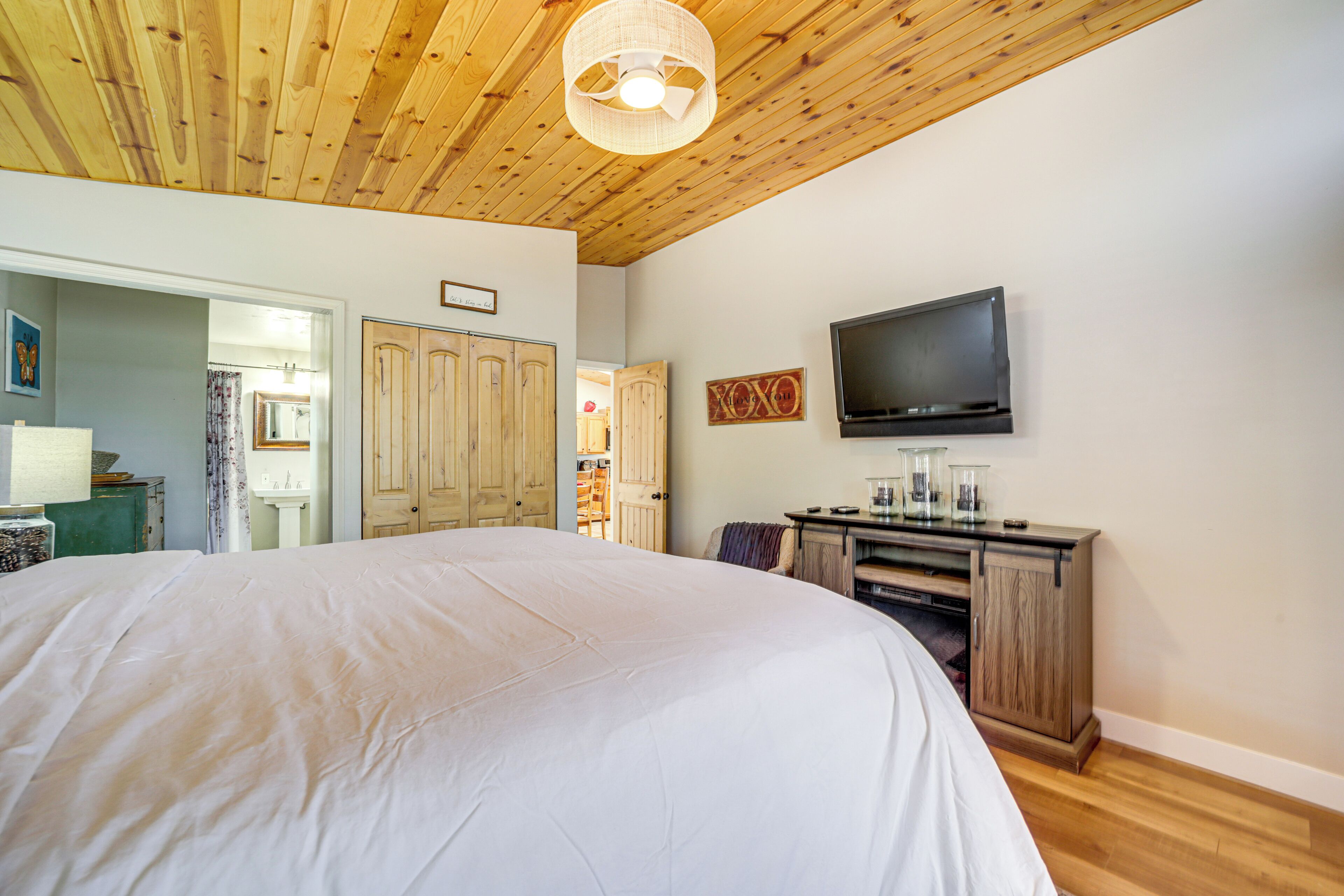 A spacious bedroom with a large bed, wooden ceiling, and a television mounted on the wall.