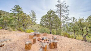 A campsite with a fire pit surrounded by wooden stumps, set in a dry, hilly area with sparse vegetation and tall trees in the background. - Strawberry Hideaway in the Pines w/ Hot Tub! (Pine)