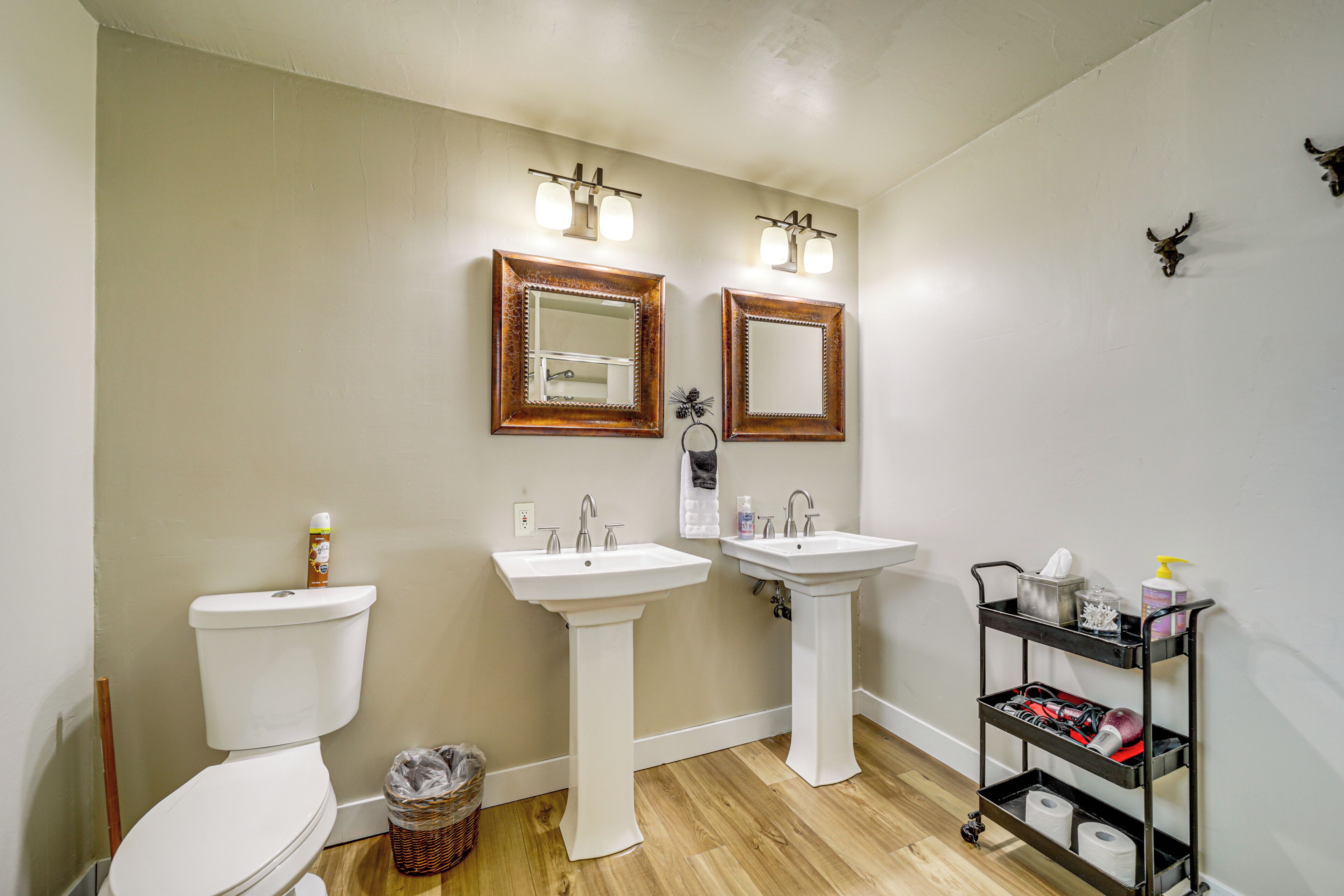 A bathroom with two sinks, a toilet, and a vanity with a mirror and lights.