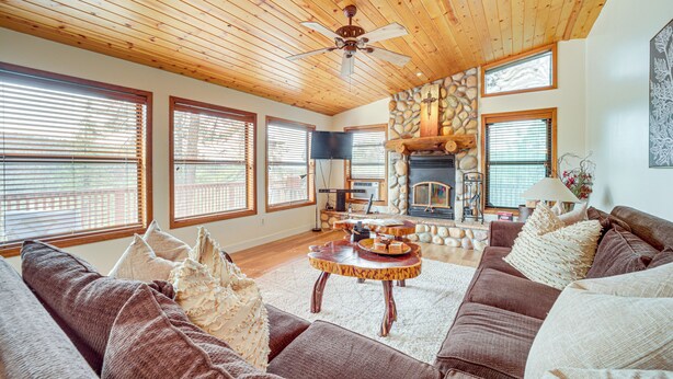 A spacious living room with a wooden ceiling, large windows, a stone fireplace, and a cozy seating area. - Strawberry Hideaway in the Pines w/ Hot Tub! (Pine)