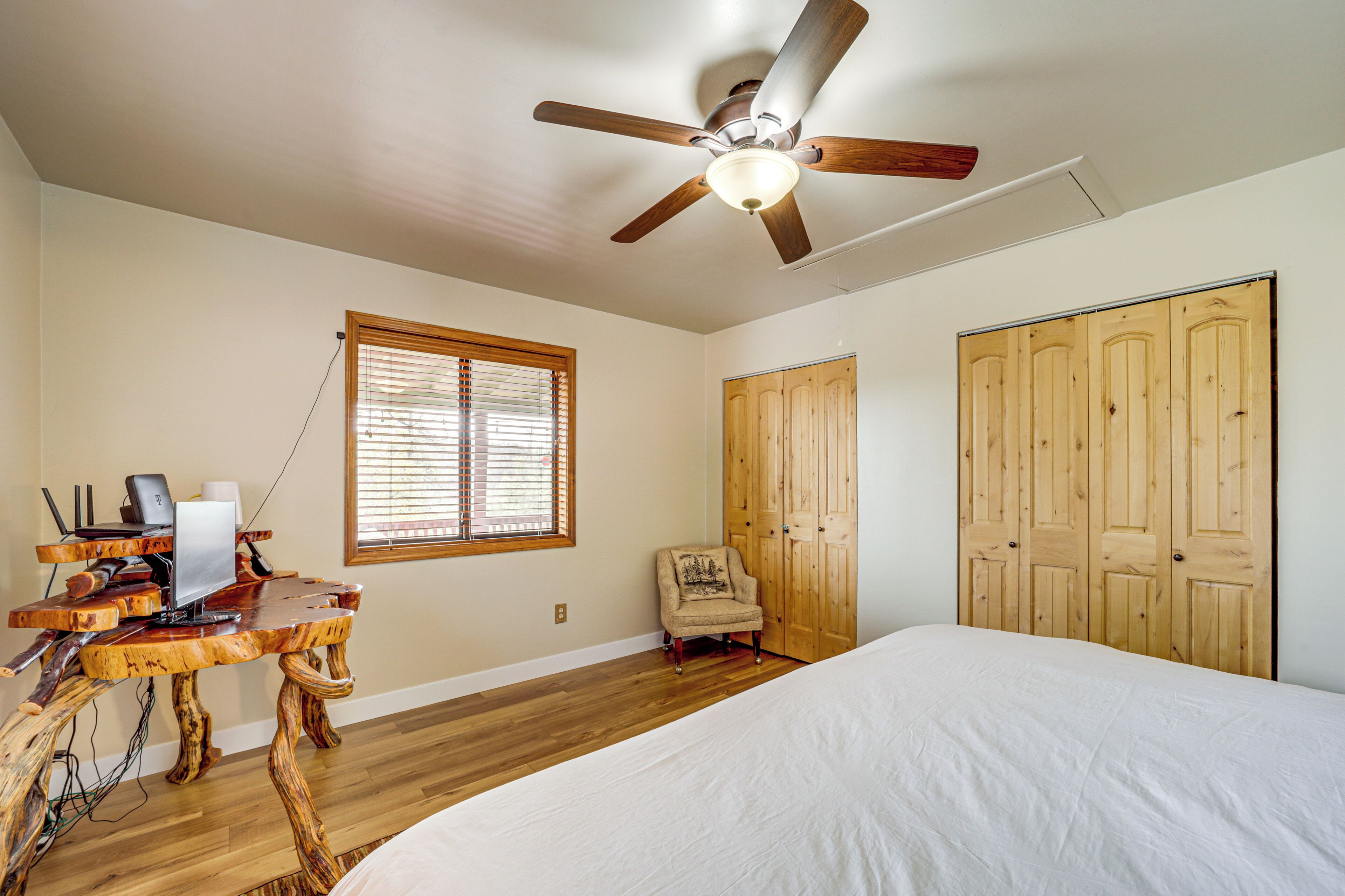 A bedroom with a bed, wooden wardrobe, a desk with a computer, and a chair.