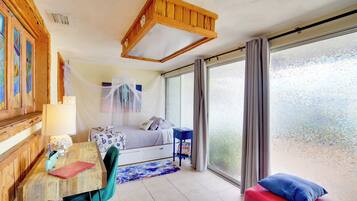 A bedroom with a bed, a desk, a chair, a window with curtains, and a wooden ceiling structure.