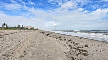 A beach with footprints, waves, and buildings in the background.