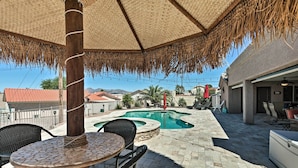 Un patio con piscina, mobiliario exterior y una sombrilla de paja.