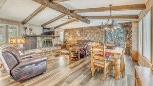 A spacious living room with a fireplace, leather recliner, dining table, and wooden beams. - Ruidoso Home w/ Hot Tub & Sierra Blanca Views (Ruidoso)