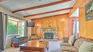 A cozy living room with a stone fireplace, wooden beams, a television, and floral-patterned furniture.