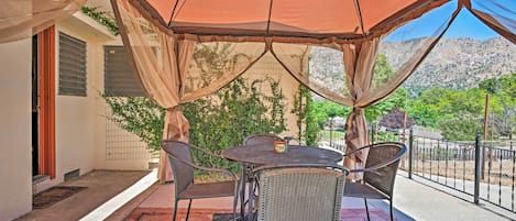 An outdoor patio with a table and chairs under a canopy, a covered walkway, and a view of a mountainous landscape.