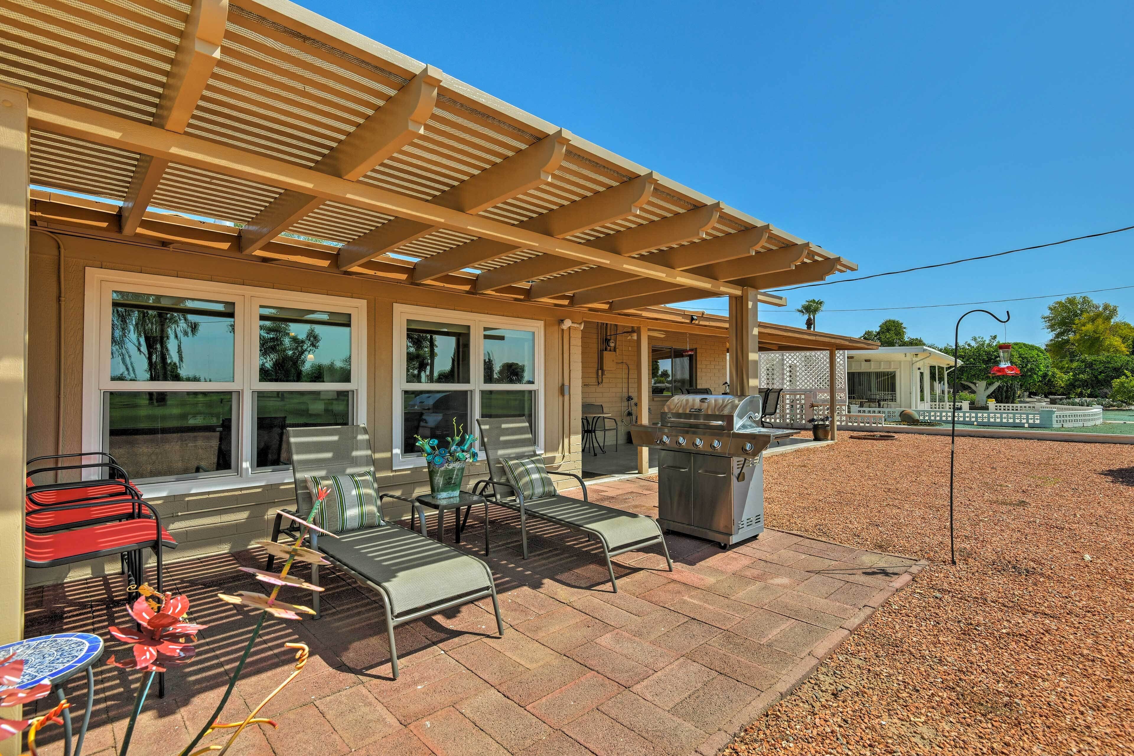 An outdoor patio with a pergola, a grill, and lounge chairs.