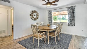 A dining area with a round table, six chairs, a ceiling fan, a wall clock, and patterned curtains. - Upscale Sun City Home on South Golf Course (Sun City)