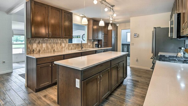 A modern kitchen with dark wooden cabinets, a large island, and pendant lighting. - Upscale Sun City Home on South Golf Course (Sun City)