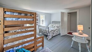 Una camera da letto con un letto a castello, un comodino con una lampada e una porta che dà su un'altra stanza.