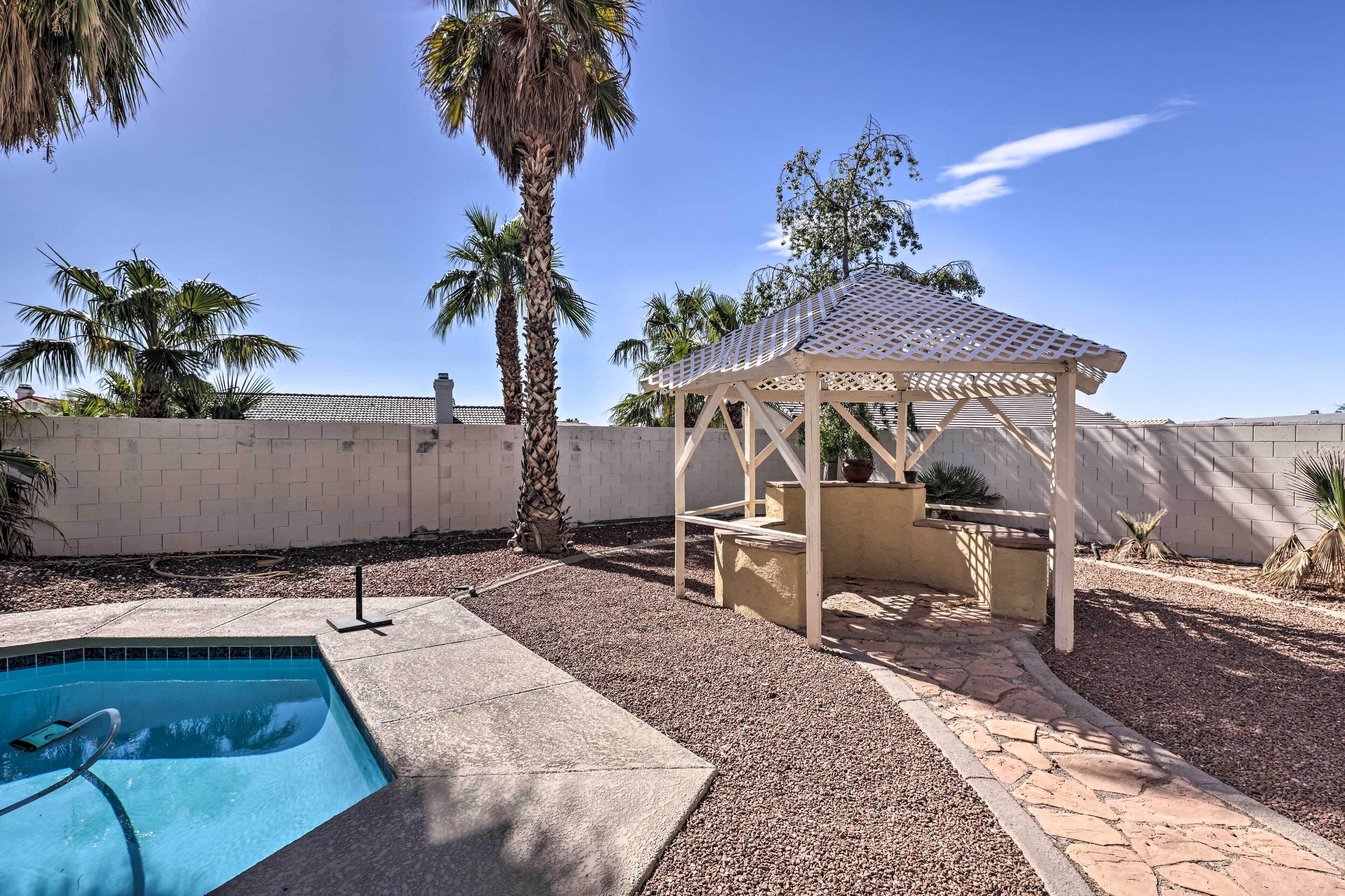 A backyard with a swimming pool, a gazebo, and palm trees.