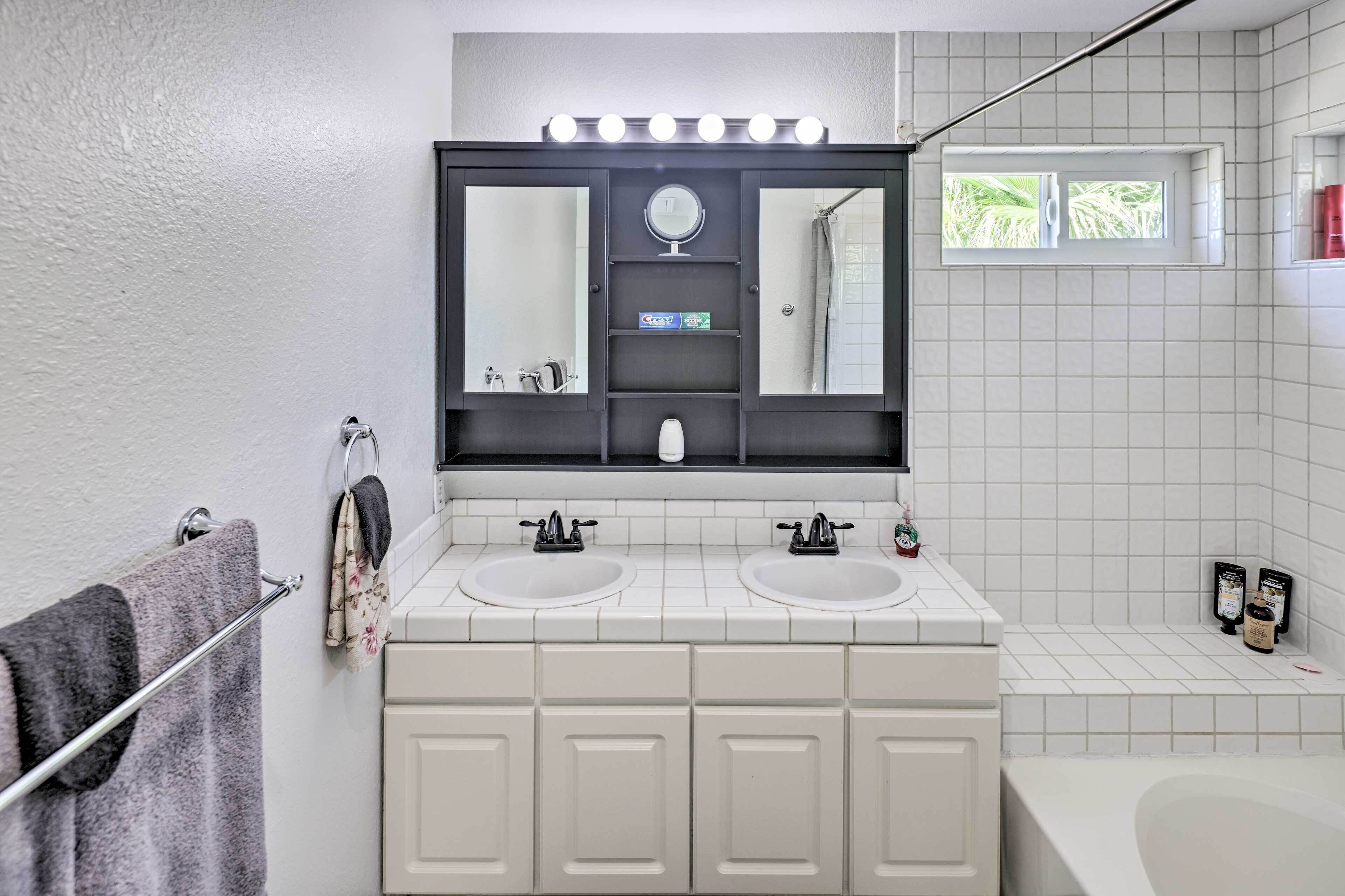 A bathroom with two sinks, a large mirror, and a window with a view of greenery.