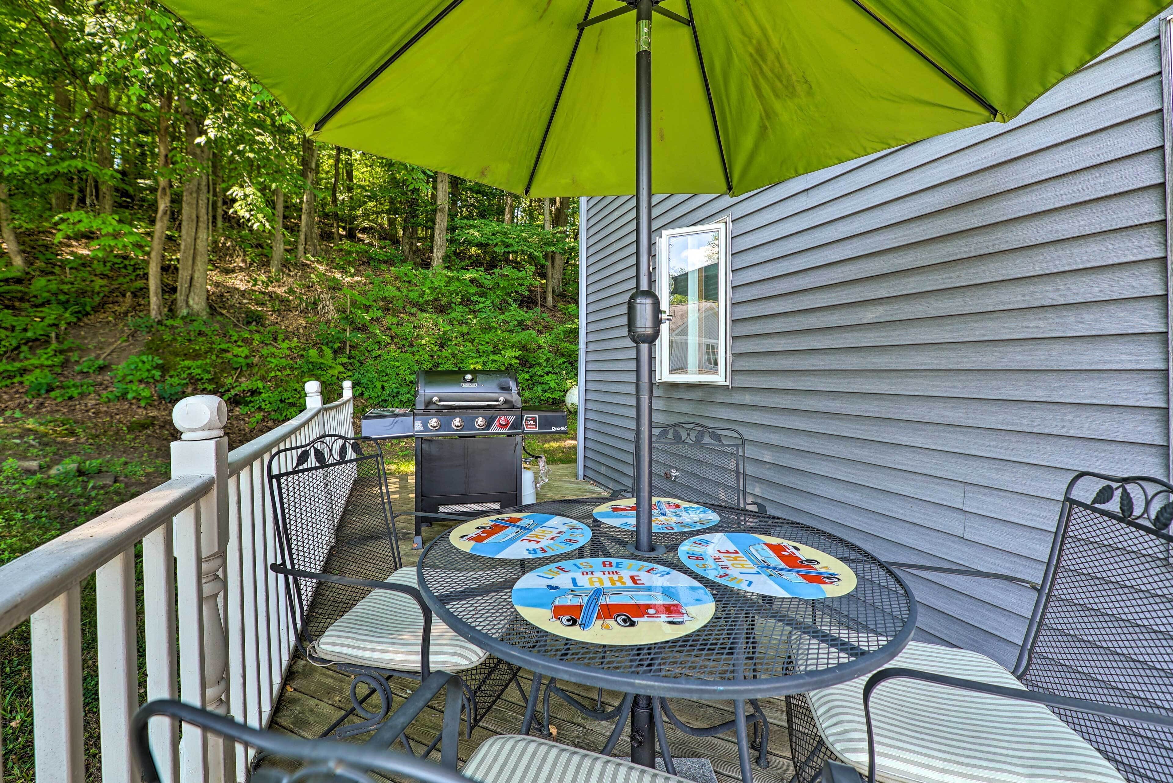 An outdoor patio with a table and chairs, a grill, and a green umbrella.