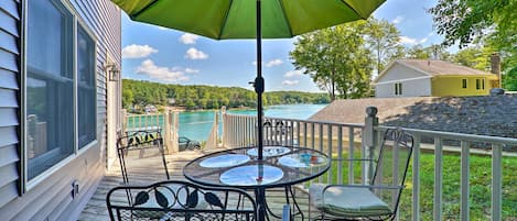 A wooden deck with a green umbrella, metal chairs, and a table.