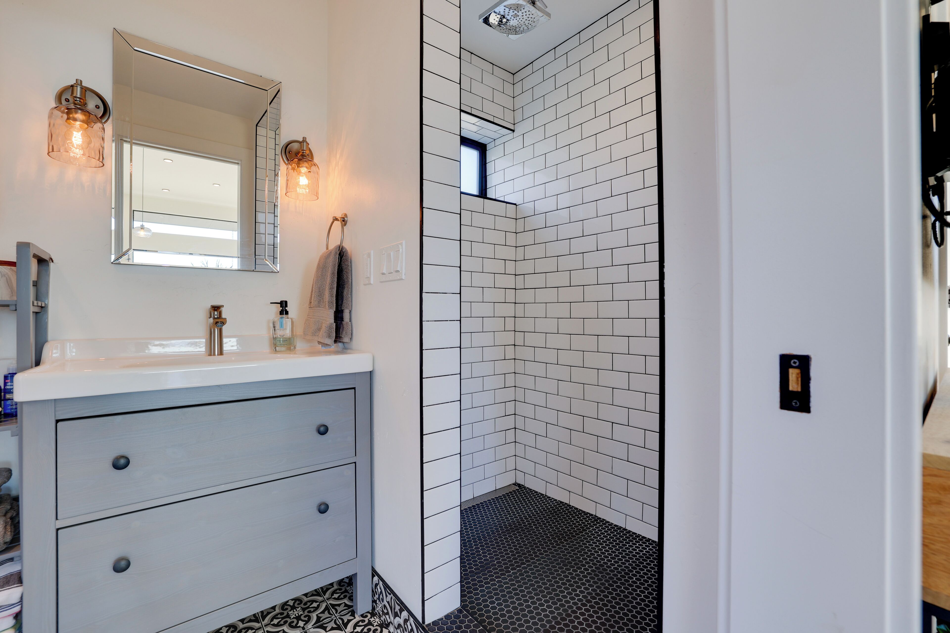 A bathroom with a white vanity, a large mirror, and a shower with white tiles.