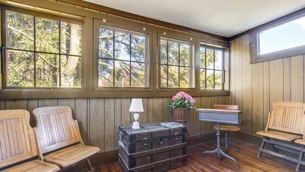 A room with wooden paneled walls, large windows, wooden benches, a desk, and a vintage suitcase. - Biking Trails, Fishing, Parks & More! Poconos Home (White Haven)